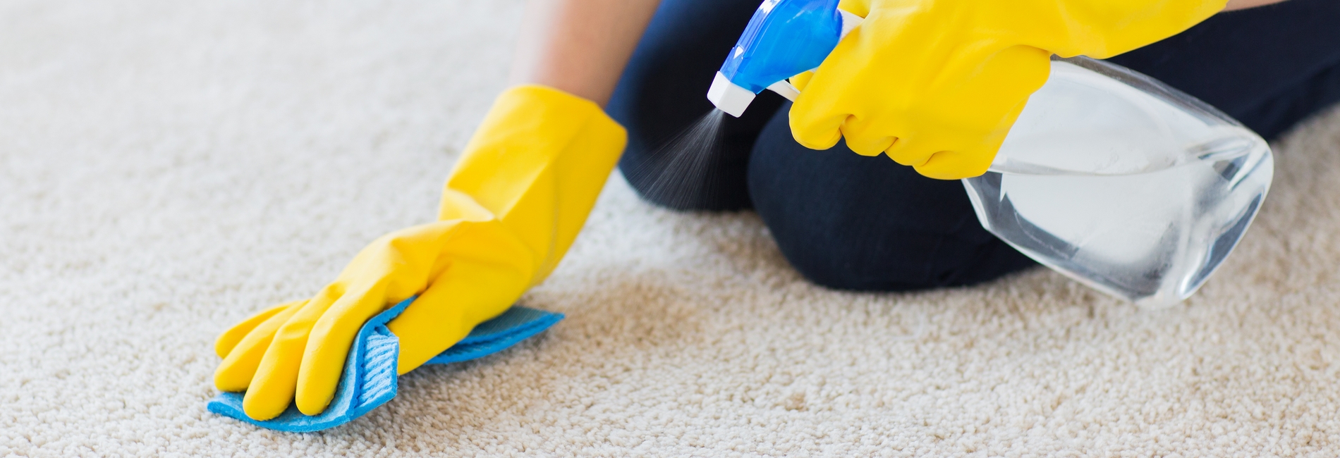 people, housework and housekeeping concept - close up of woman in rubber gloves with cloth and detergent spray cleaning carpet at home